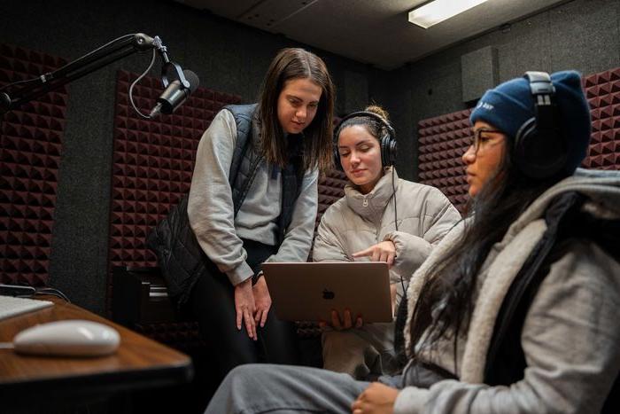 3 female college students sit in a podcasting booth 