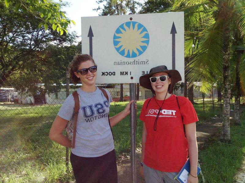 两名宾州州立大学的学生在一个指向巴拿马史密森热带研究所的标志前摆姿势.
