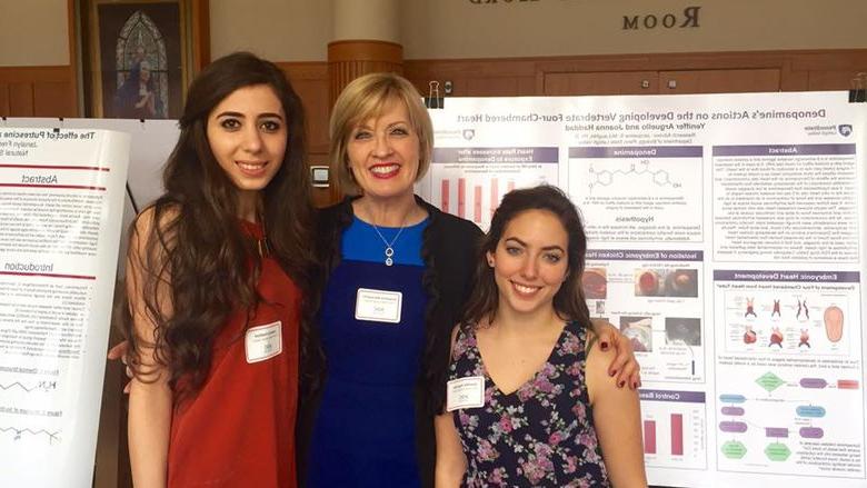 Two students pose with professor in front of their research project